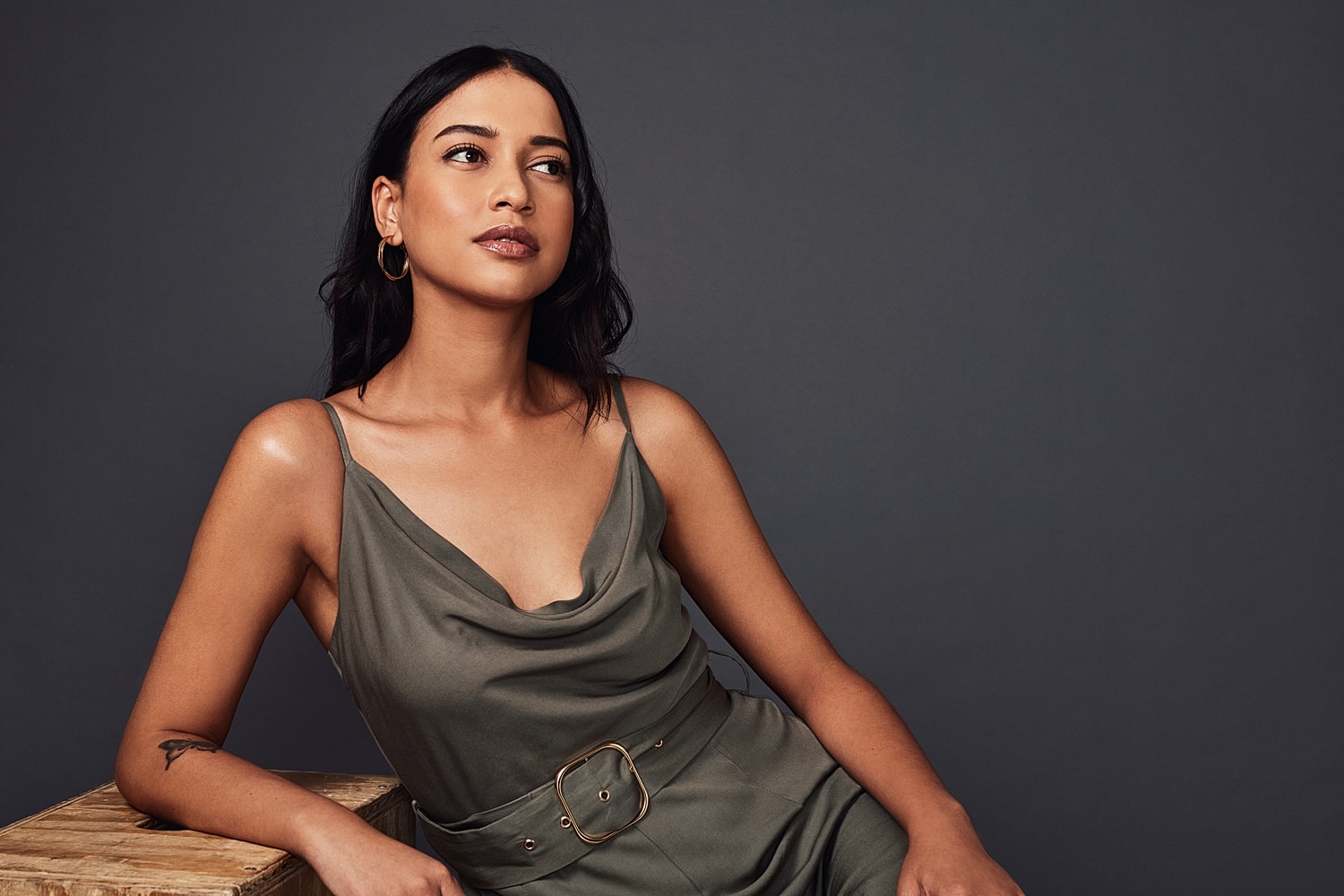 Woman in olive dress posing against dark background.