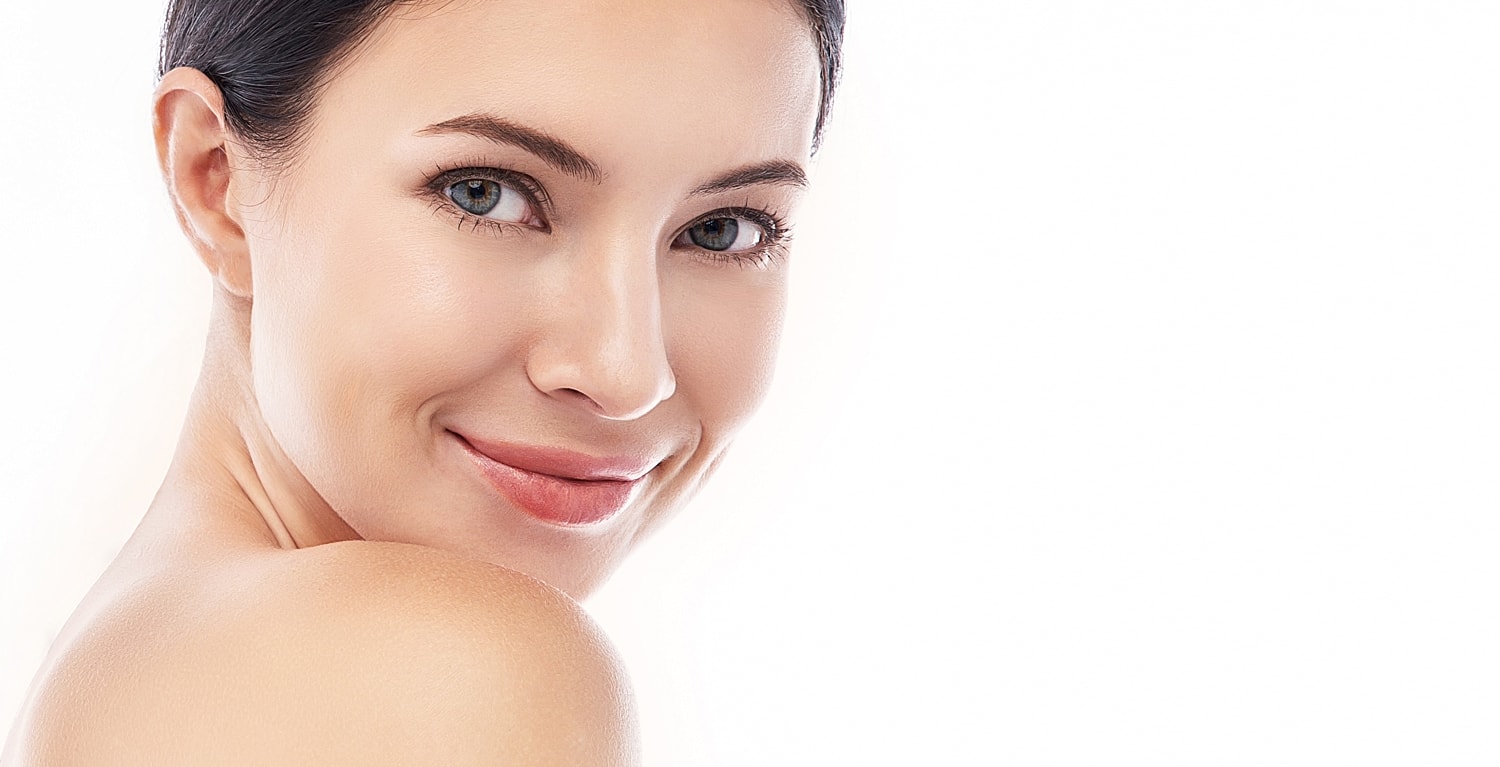 Smiling woman with clear skin, minimalist background.